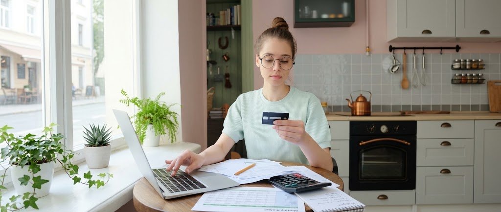 Young adult with a first credit card planning how to build credit from scratch at a laptop