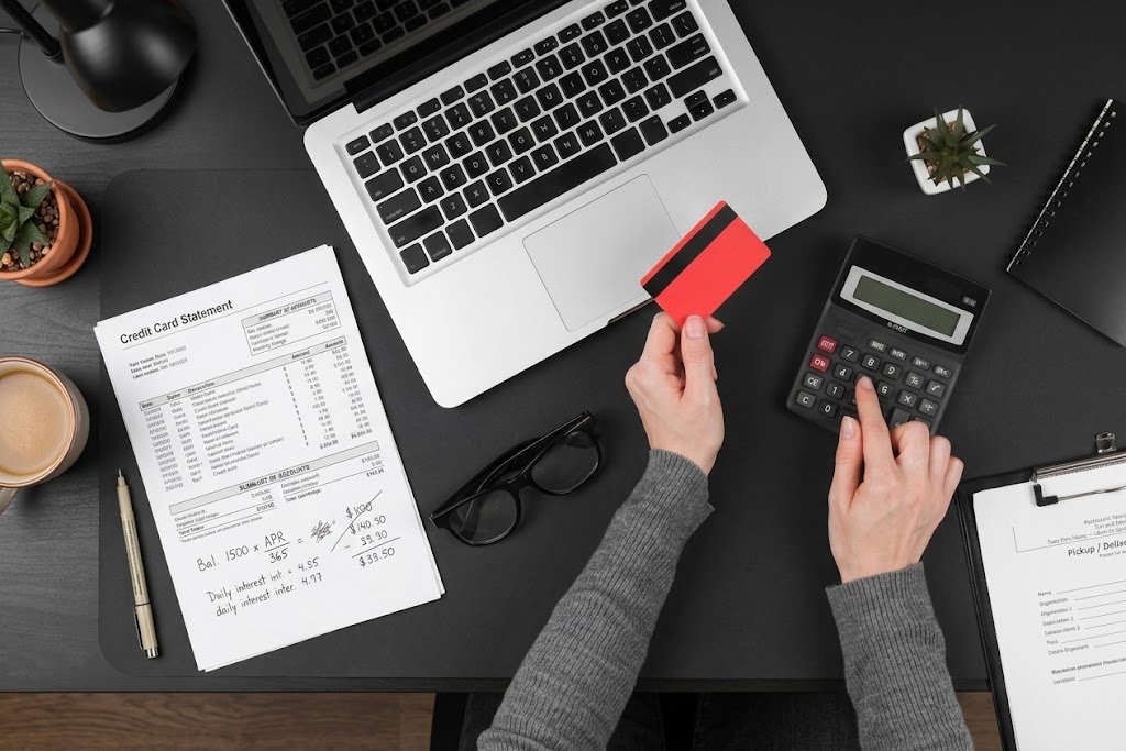 Person using a calculator next to a credit card statement, representing how credit card interest is actually calculated