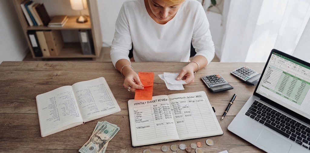 Person completing a monthly money review at a desk with a laptop, notebook, and coffee