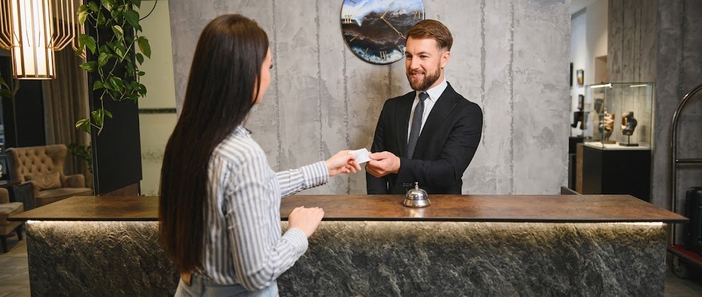Traveler handing a credit card to a hotel front desk clerk, illustrating pre-authorization holds on a card
