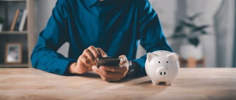 Smartphone showing a round-up savings balance from micro-savings apps next to a small piggy bank