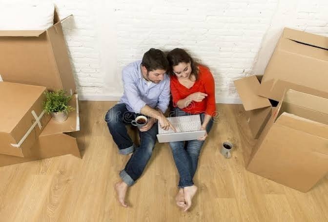 Couple comparing cost of living and salary offers next to moving boxes before relocating