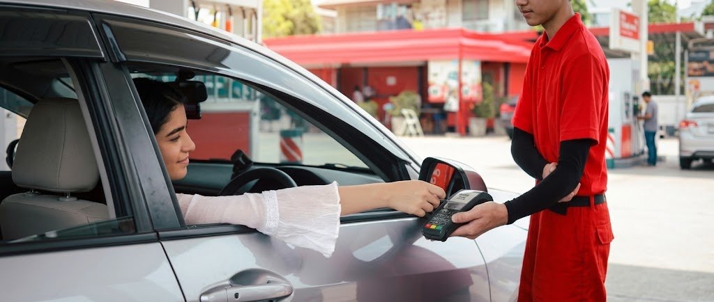 Driver paying at a gas pump to get fuel surcharge waivers and card rewards
